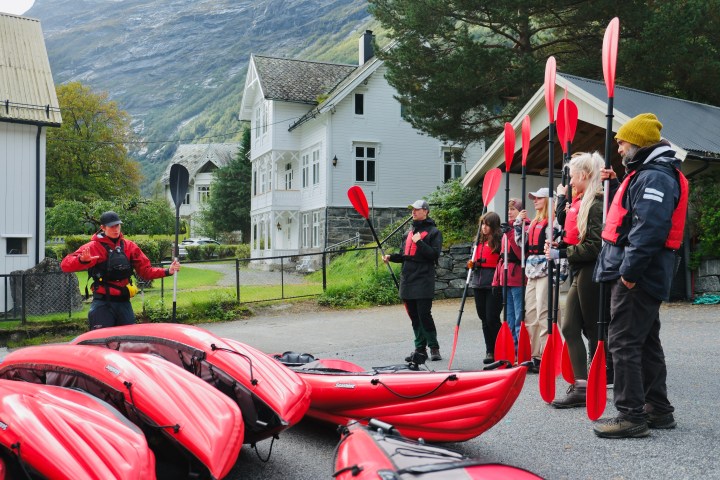 Group of people in life vests holding paddles near red kayaks with a guide in outdoor setting.