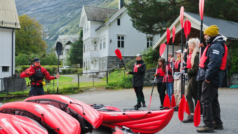 Group of people in life vests holding paddles near red kayaks with a guide in outdoor setting.