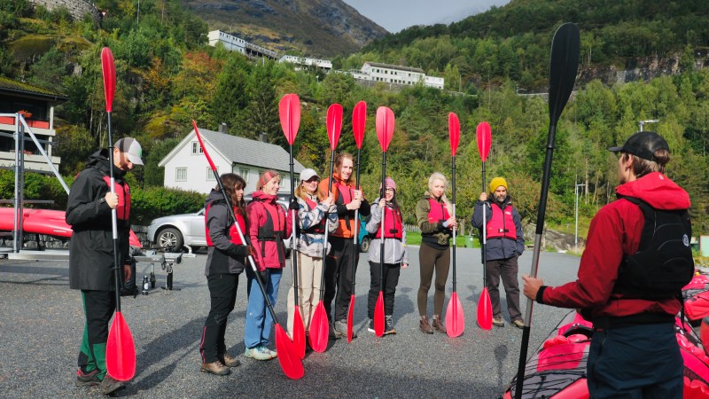 Group of people standing with red kayak paddles during outdoor lesson, mountains in background.