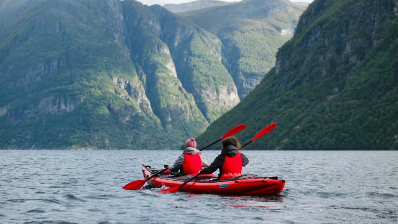 Two people kayaking in a red kayak on a lake surrounded by mountains.