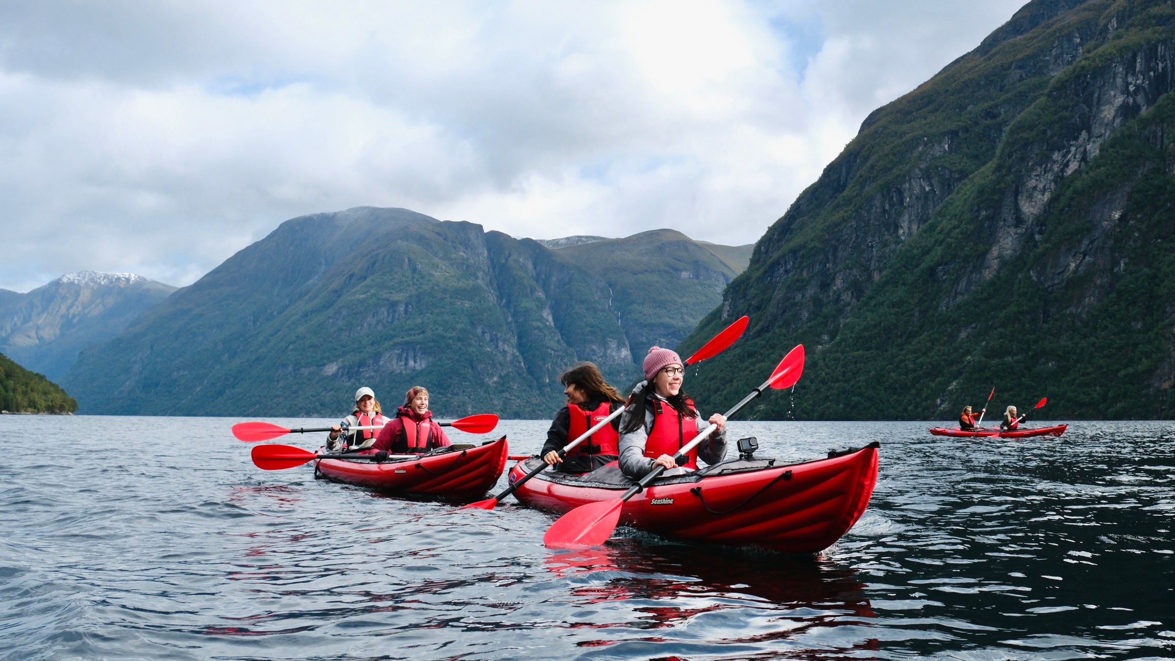People kayaking in red kayaks on a lake surrounded by mountains.
