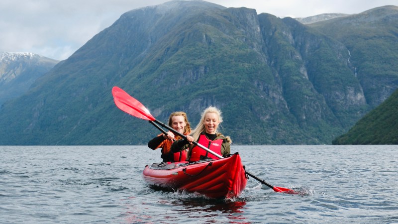 Two people kayaking in a red kayak on a lake with mountains in the background.