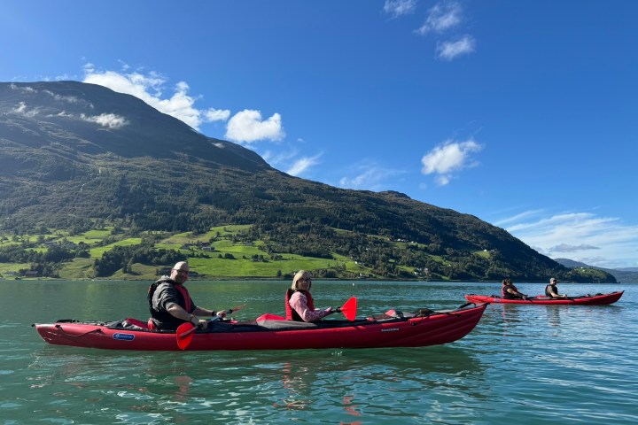 People kayaking on a lake with mountains and blue sky in the background.