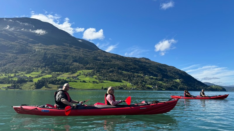 People kayaking on a lake with mountains and blue sky in the background.