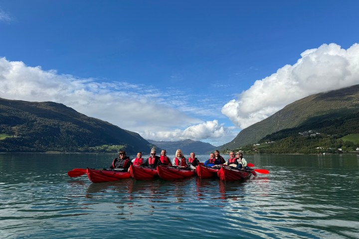Group kayaking on calm lake with mountains and cloudy sky in background.