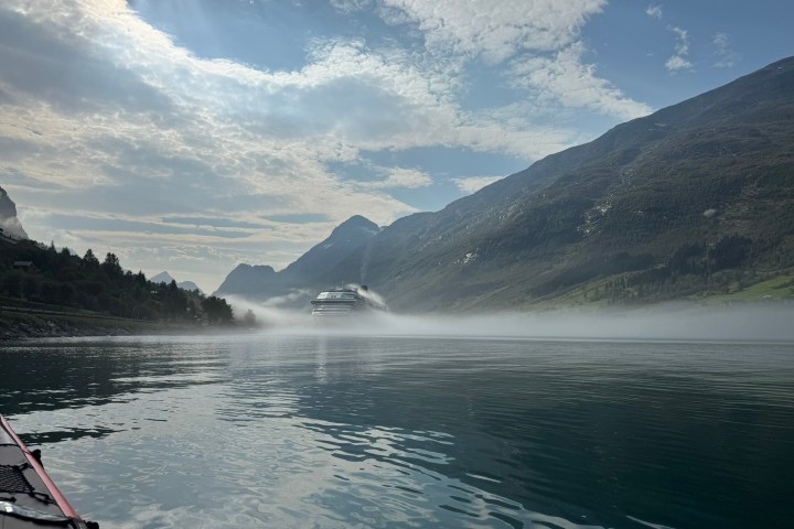 Cruise ship in misty fjord surrounded by mountains under cloudy sky.