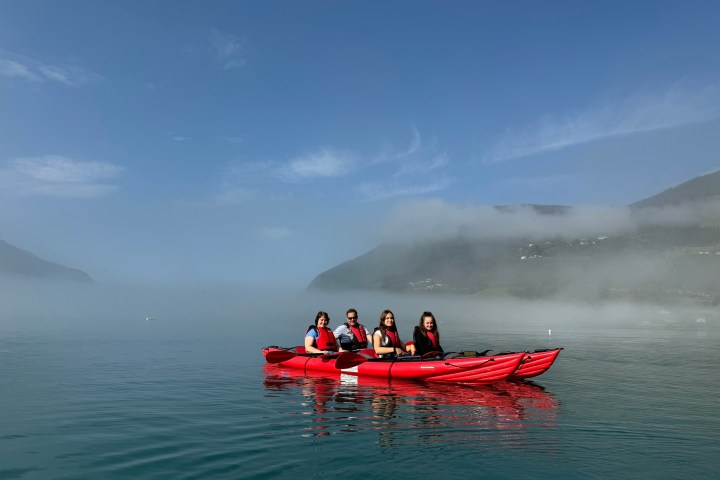 Four people kayaking on calm lake with misty mountains in the background.