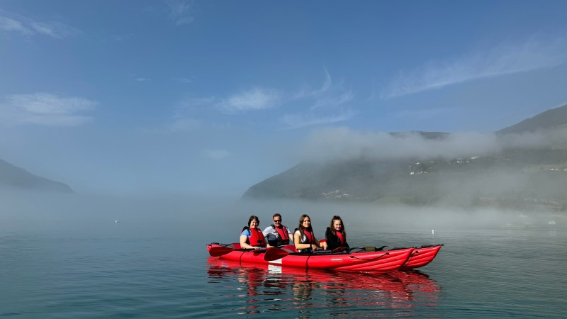 Four people kayaking on calm lake with misty mountains in the background.